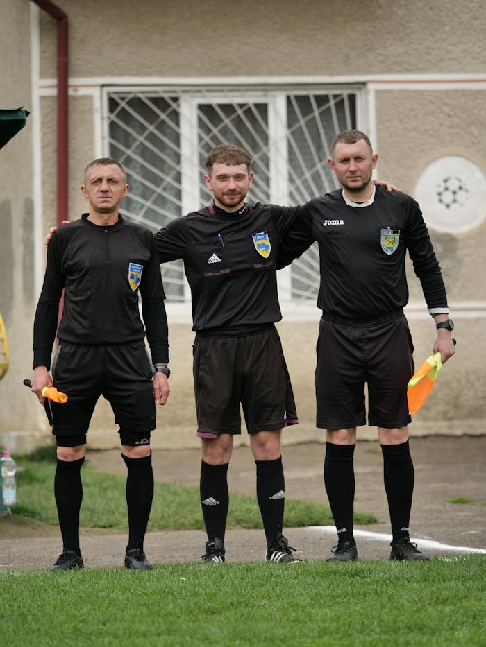 Three referees in black jerseys standing together on the soccer field.